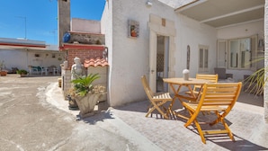 A patio with a table and chairs, a small garden area with potted plants, and a building with a tiled roof and a satellite dish. - 2432 Tenuta Fioravante - Bilo Antonia by Barbarhouse (Porto Cesareo)