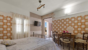 A bedroom with a bed, a TV, a dining table with chairs, and patterned walls. - 2432 Tenuta Fioravante - Bilo Antonia by Barbarhouse (Porto Cesareo)