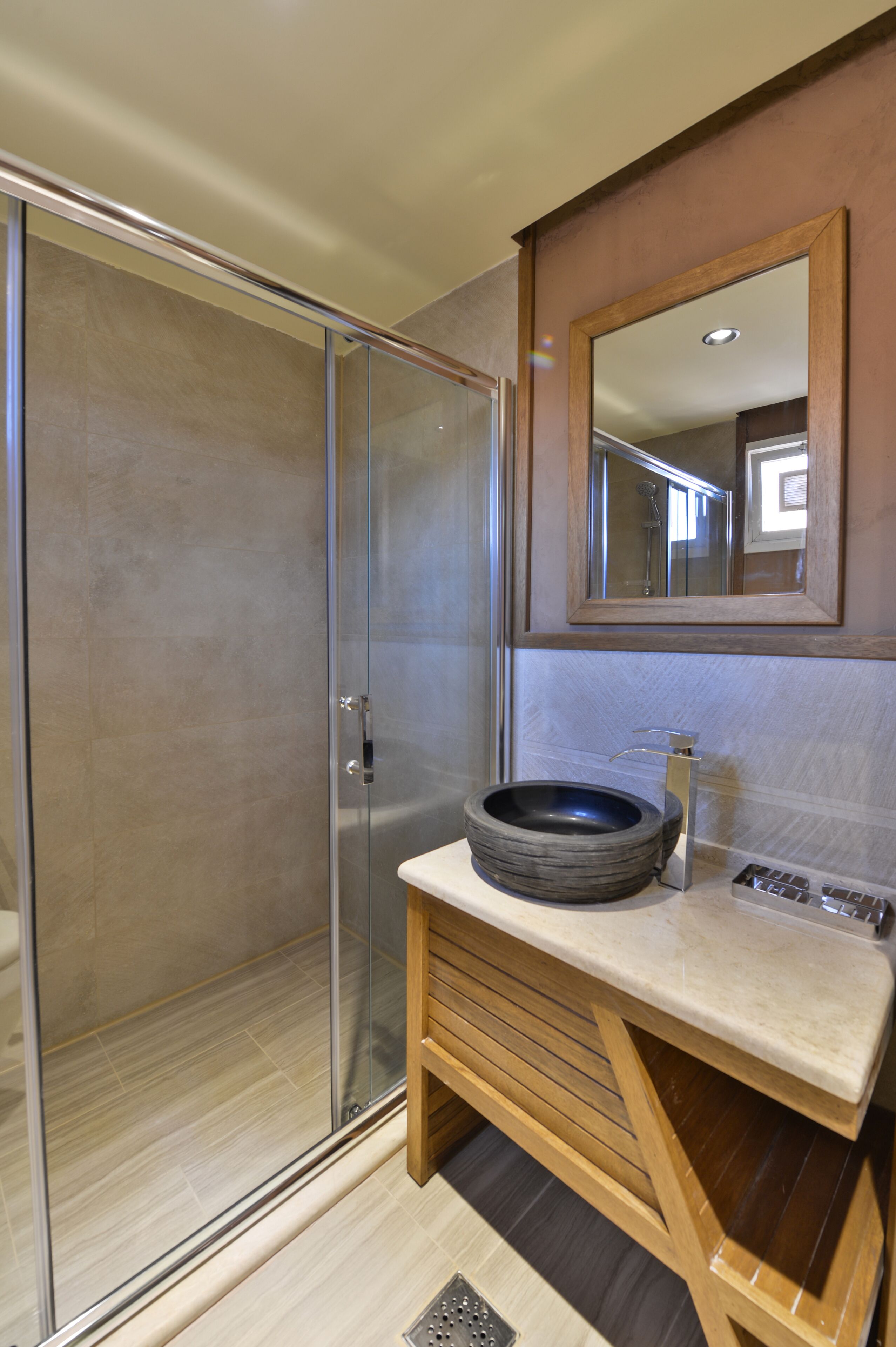 A bathroom with a glass shower enclosure, a wooden vanity with a sink, and a mirror above the vanity.