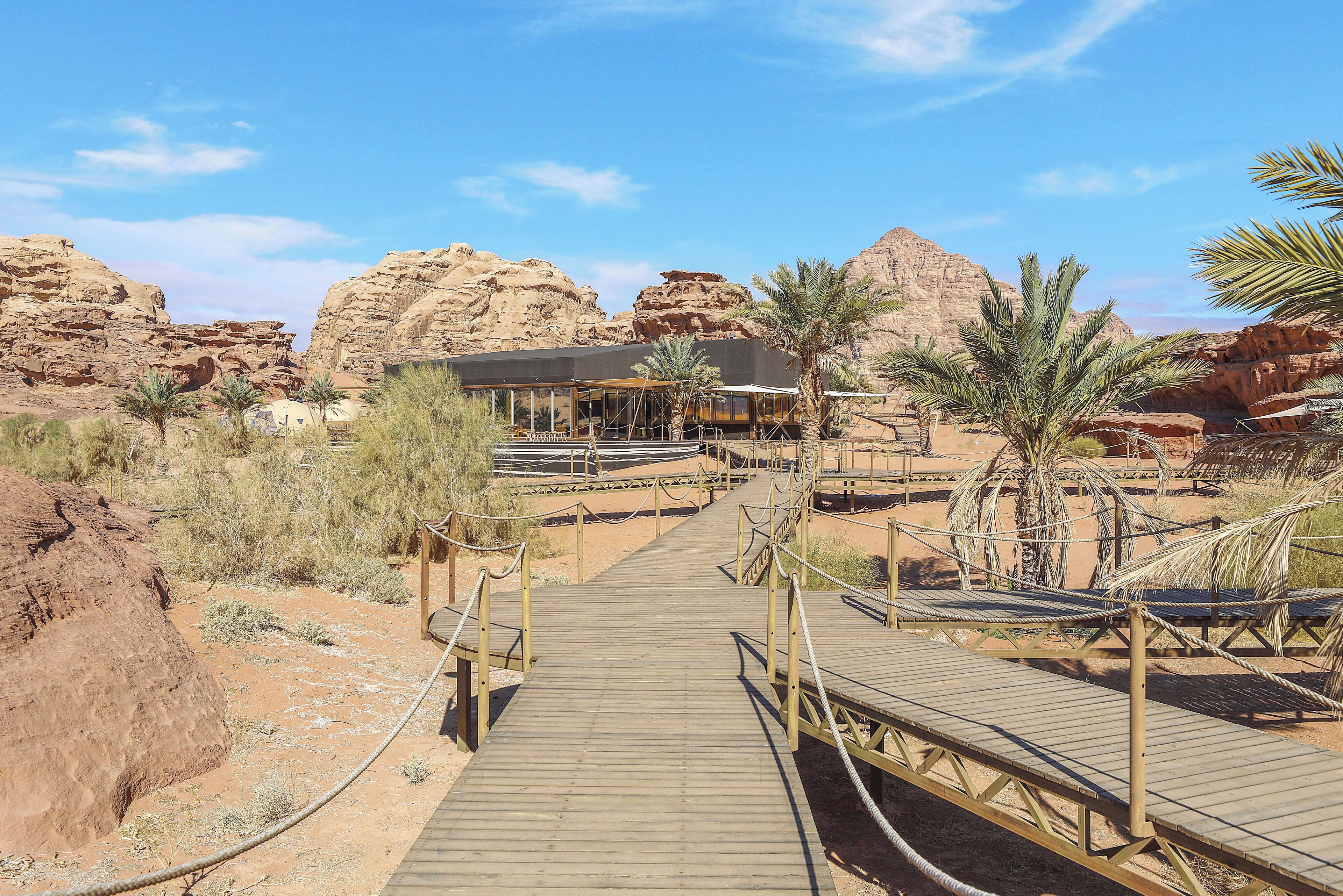 A desert resort with a wooden boardwalk leading to a building with a flat roof and a covered area.