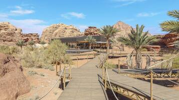 A desert resort with a wooden boardwalk leading to a building with a flat roof and a covered area.