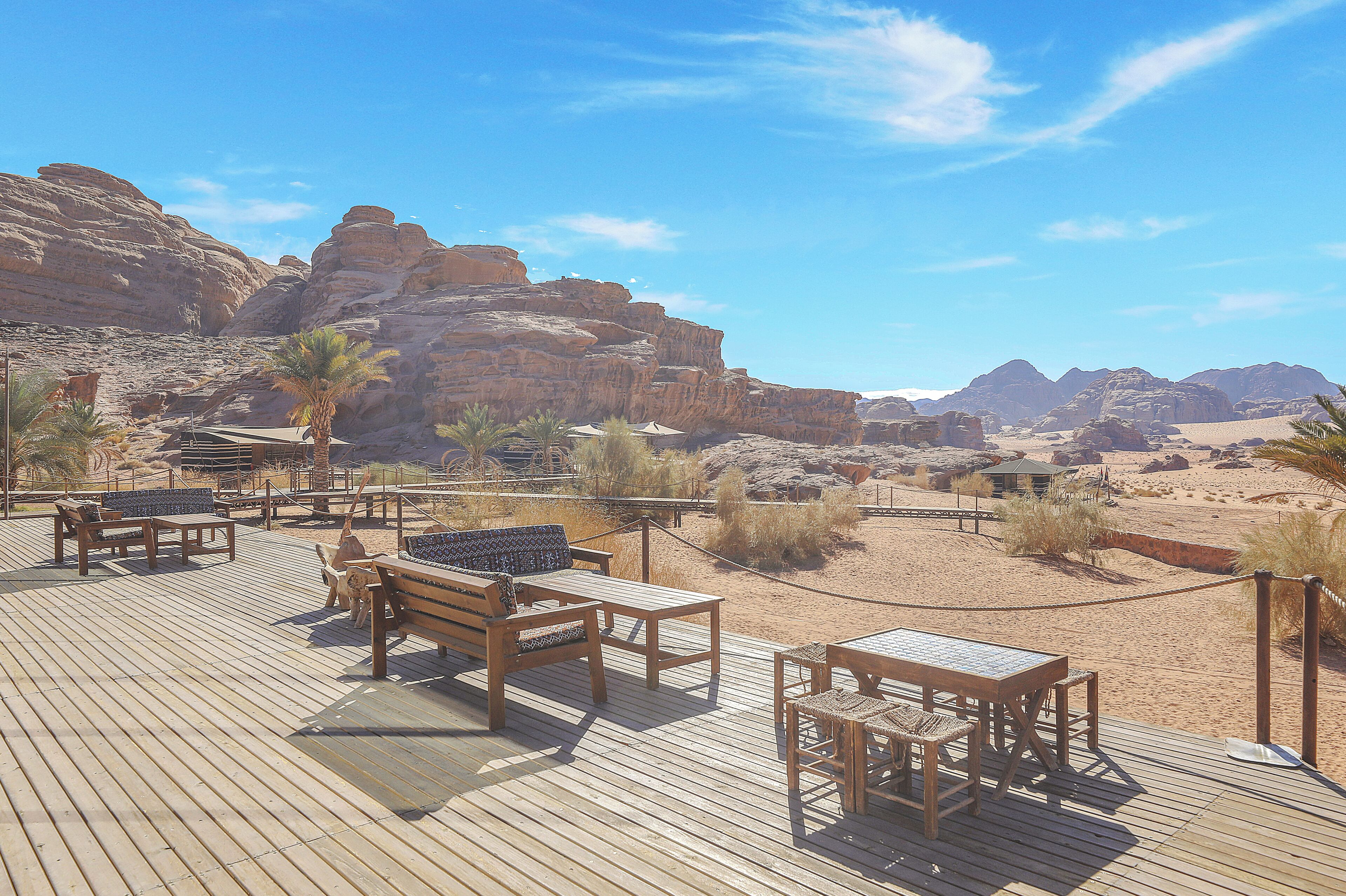 A wooden deck with outdoor furniture, a palm tree, and a view of desert mountains.