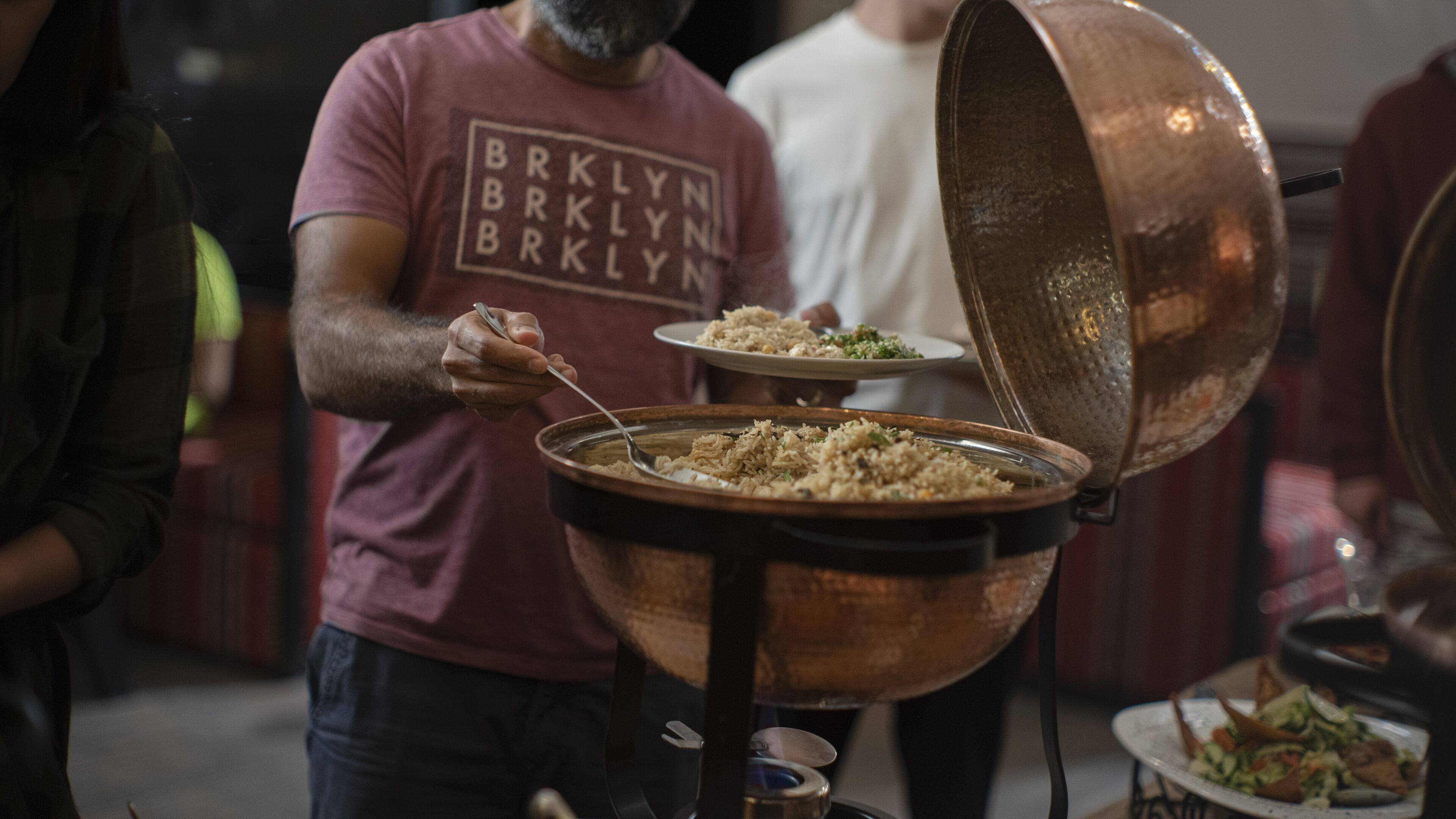 A person serving food from a large copper pot.