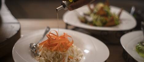 A hand pouring oil over a dish of shredded vegetables.