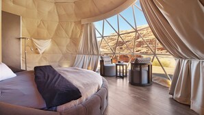 Una habitación tipo tienda espaciosa con una cama grande, una mesita pequeña y vistas a un paisaje rocoso.