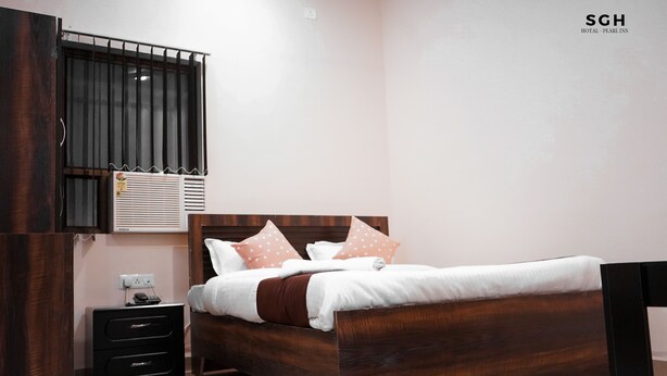 Un dormitorio con una cama de madera, una mesita de noche, aire acondicionado instalado en la pared y una ventana con barrotes.