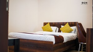 Una cama bien hecha con estructura de madera, dos almohadas y una silla a un lado.