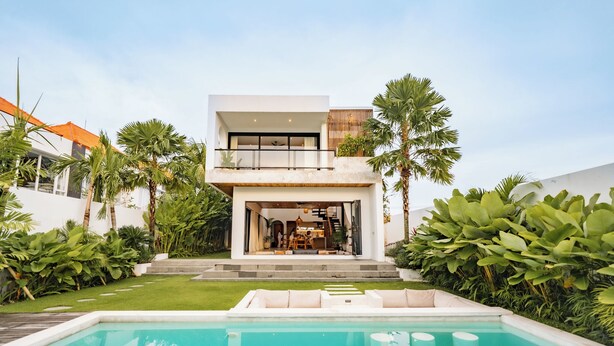 Een modern huis met twee verdiepingen, met een zwembad, omringd door weelderige begroeiing.