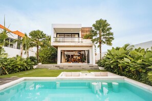 Une maison moderne à deux étages avec une piscine, entourée d’une végétation luxuriante.