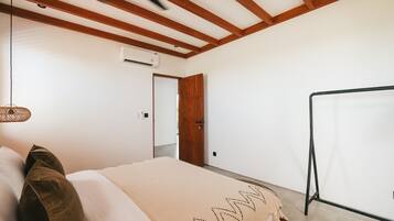A bedroom with a bed, wooden ceiling beams, a hanging light fixture, and a door leading to another room.