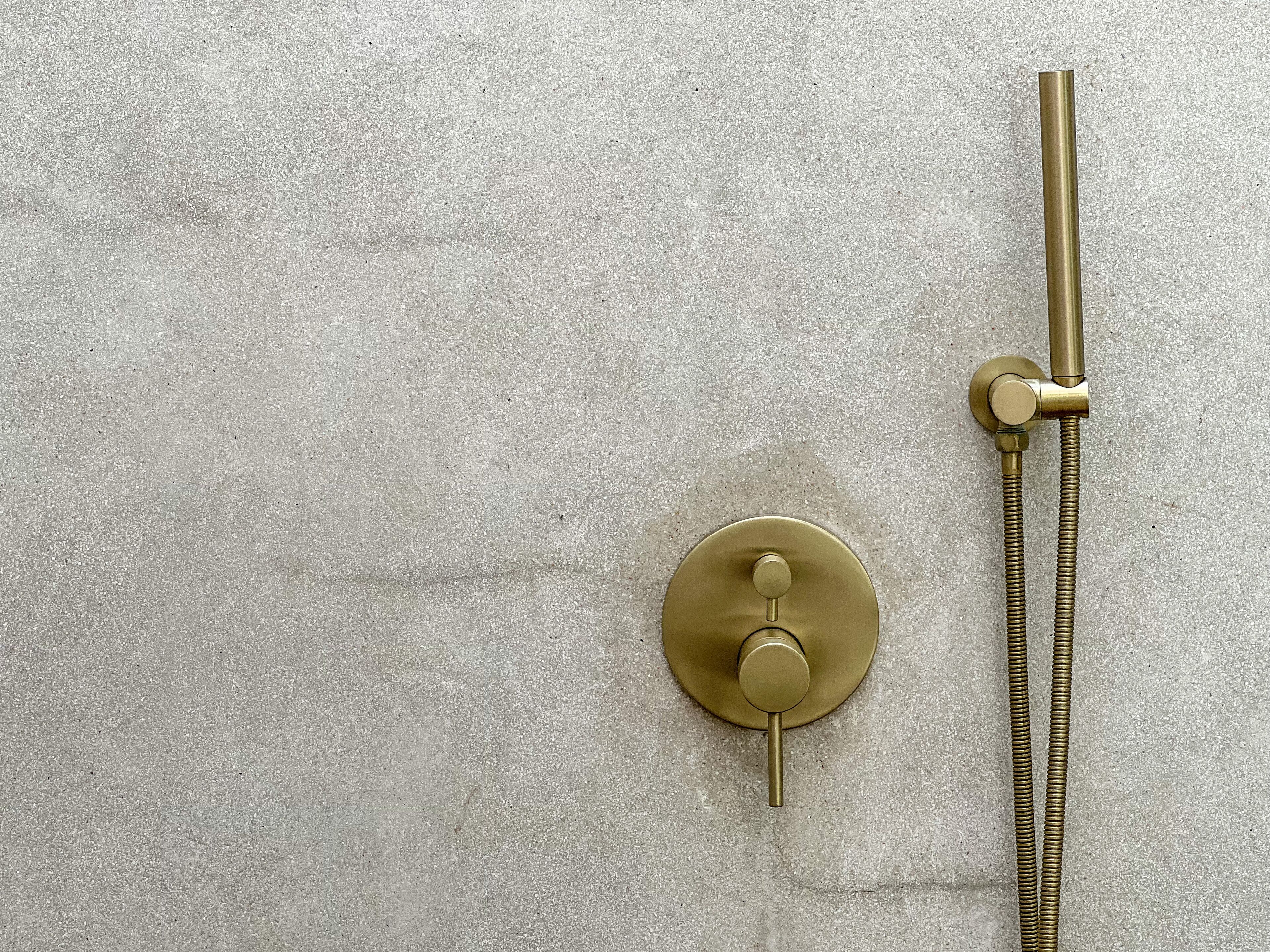 Un cabezal de ducha de latón con una manguera flexible frente a una pared con relieve.