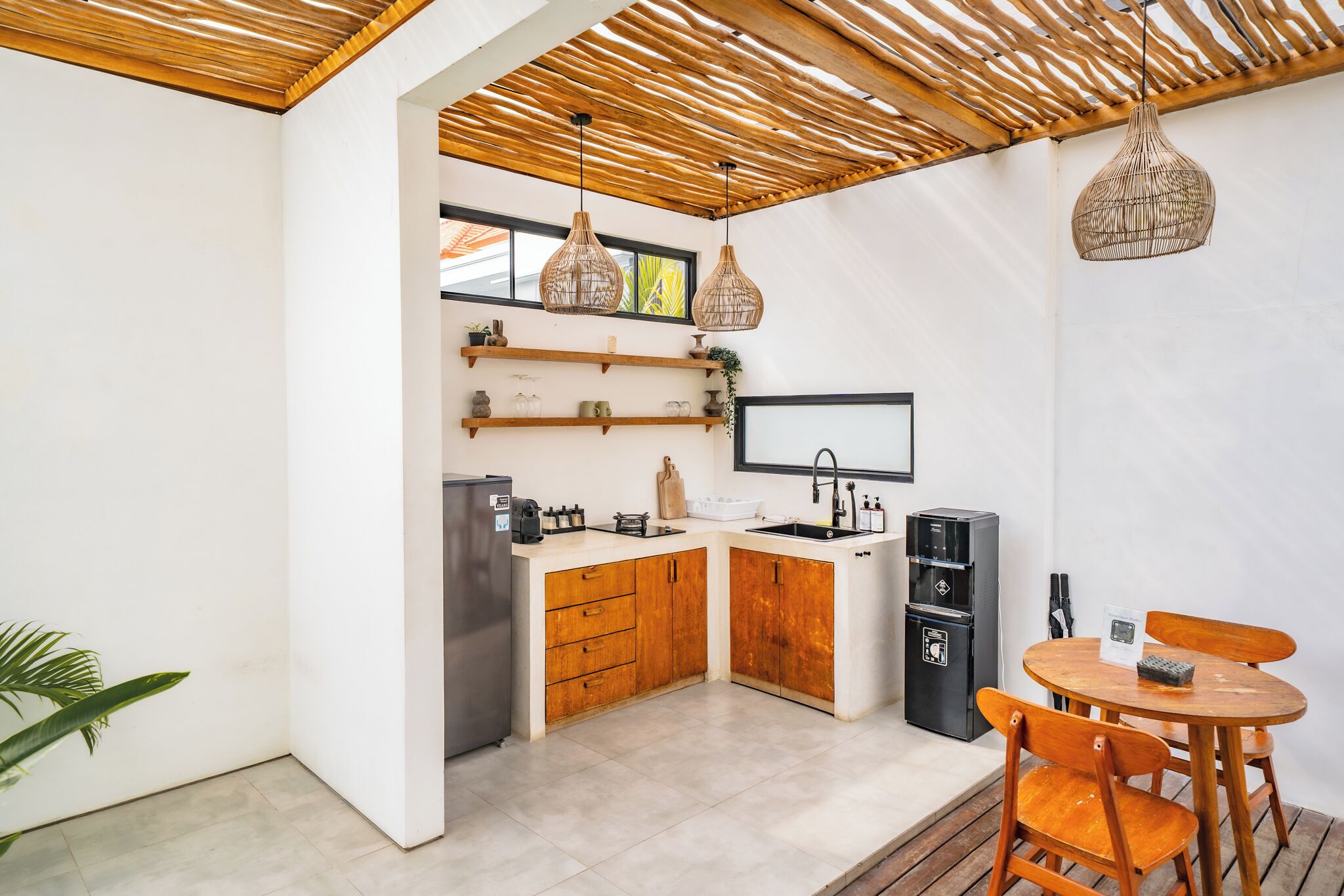 Een kleine keuken met houten kastjes, een koelkast, een spoelbak en een eethoek met een tafel en stoelen.