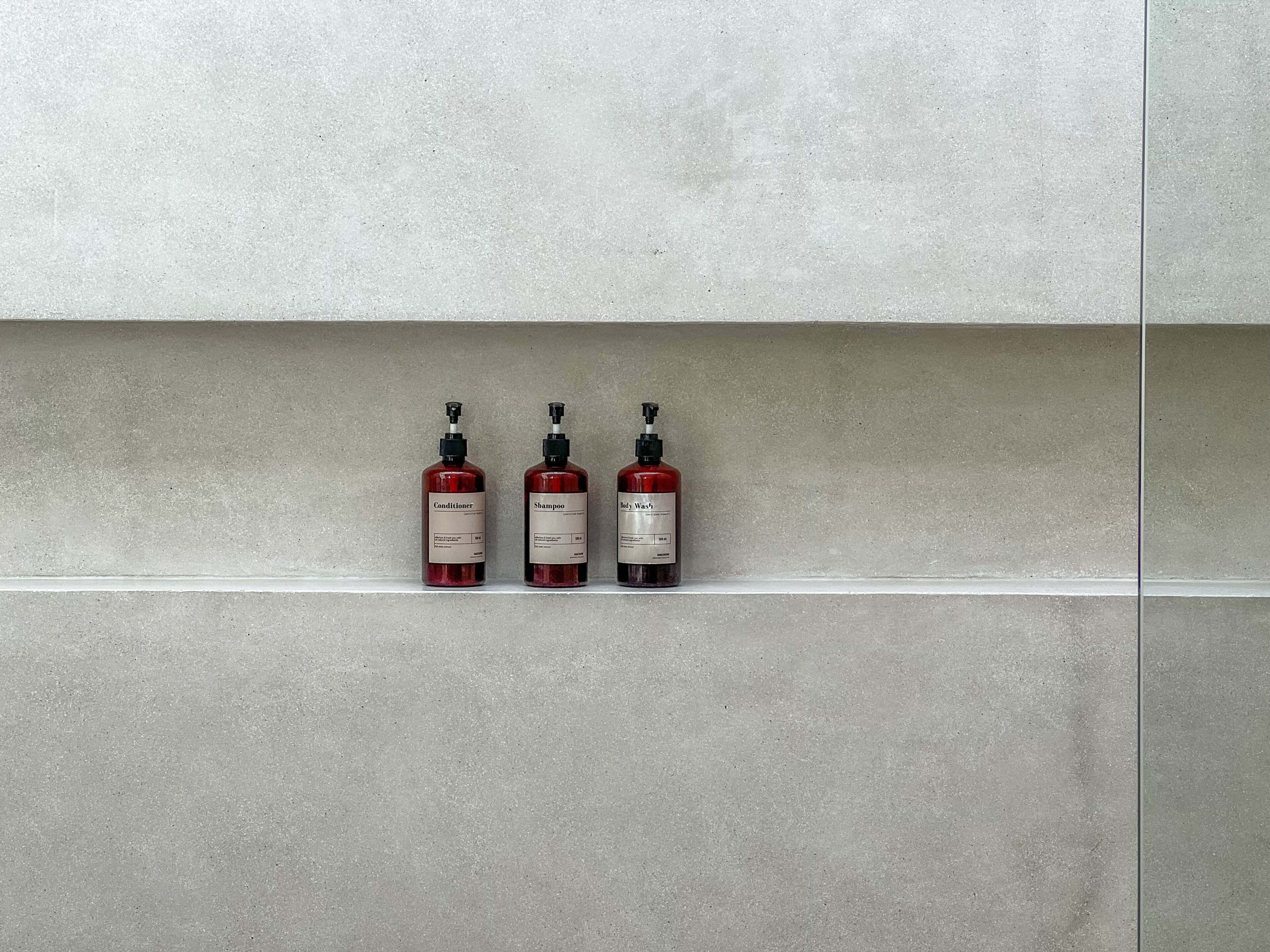 Tres botellas de líquido sobre una estantería frente a una pared lisa.