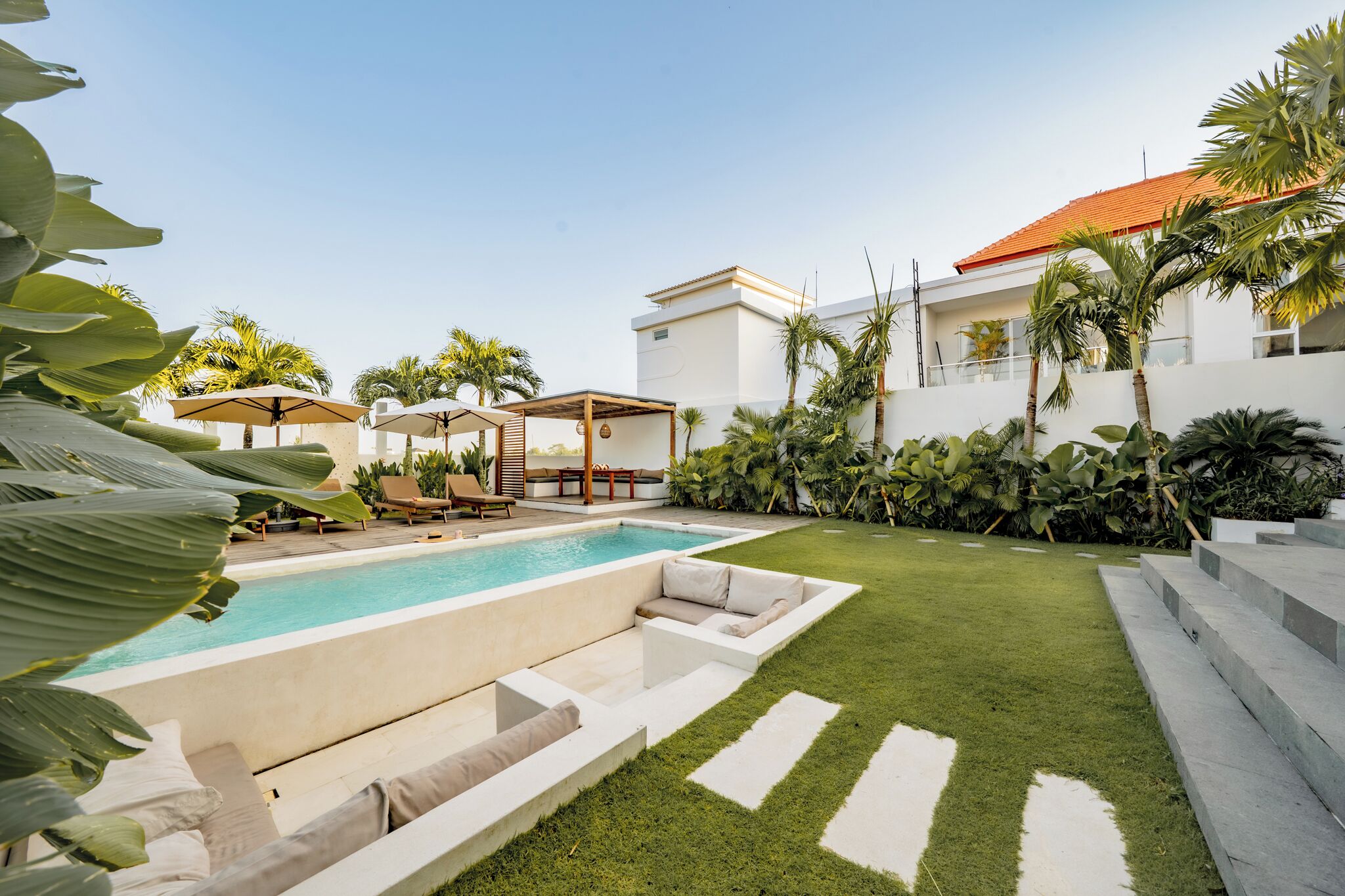 Ein moderner Poolbereich mit Liegestühlen, einer überdachten Lounge und einem gepflegten Rasen.