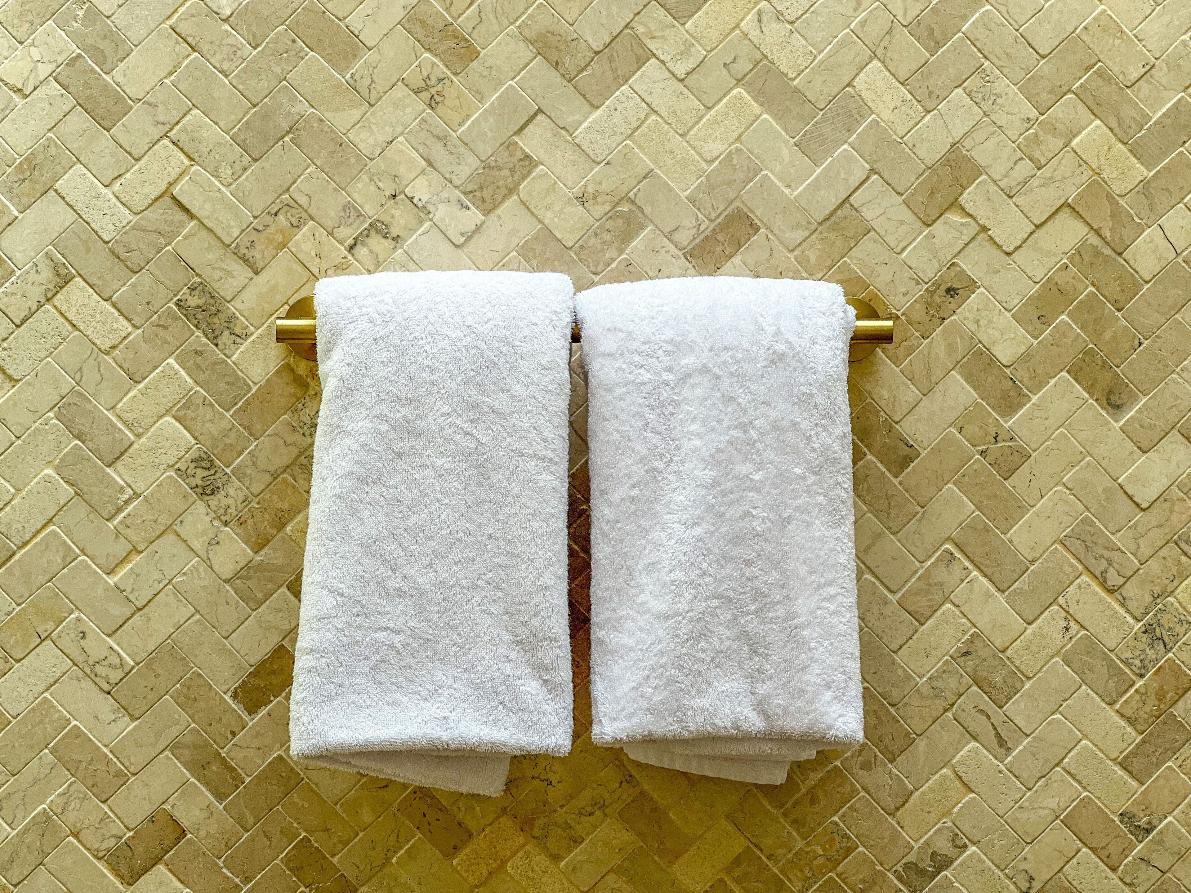 Two white towels hanging on a golden towel rack against a herringbone-patterned tiled wall.