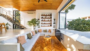 Een moderne woonkamer met een visgraatvloer, een plafondventilator, een trap en een groot raam met uitzicht op een tuin.