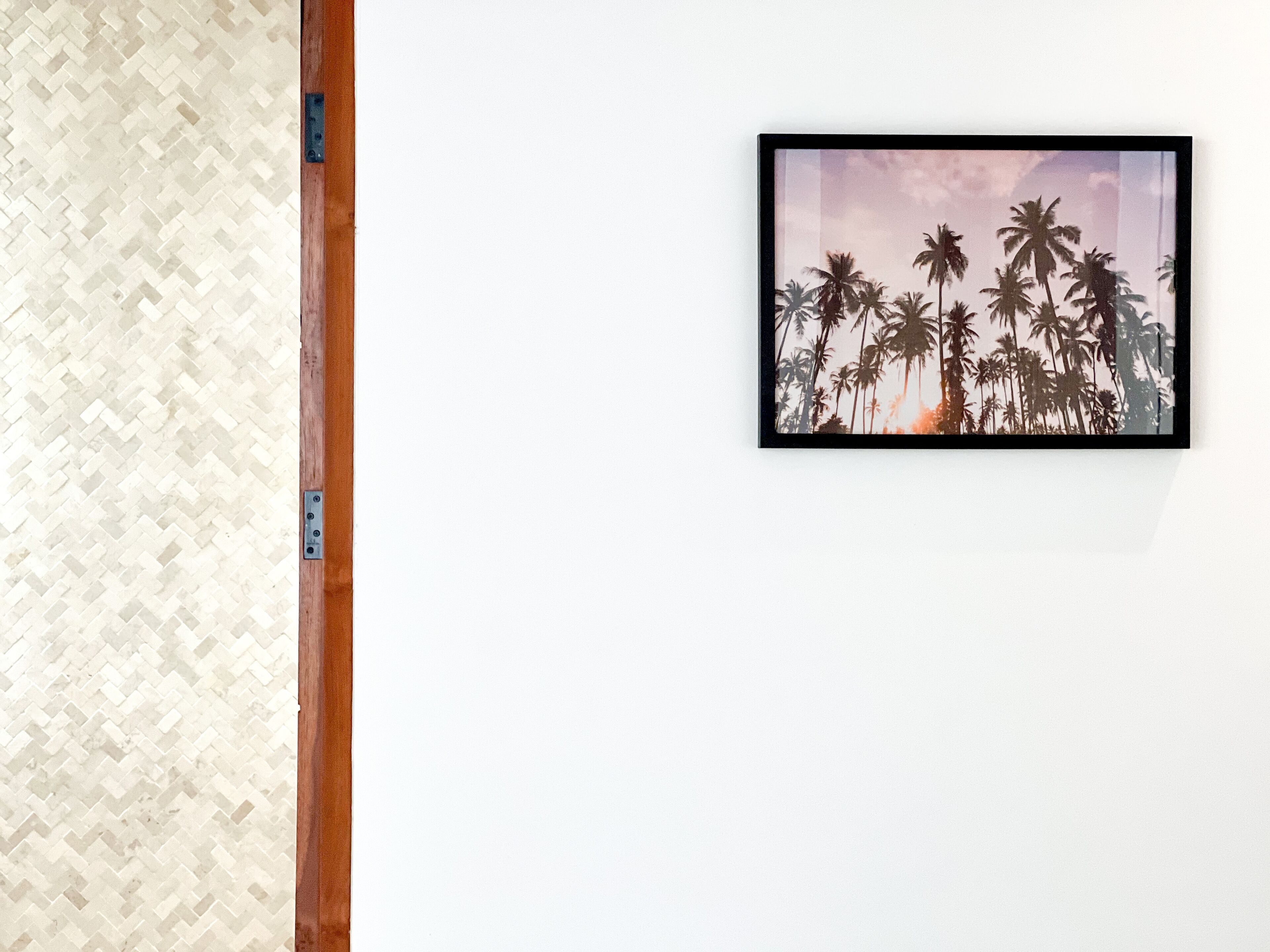 A framed picture of palm trees on a white wall.