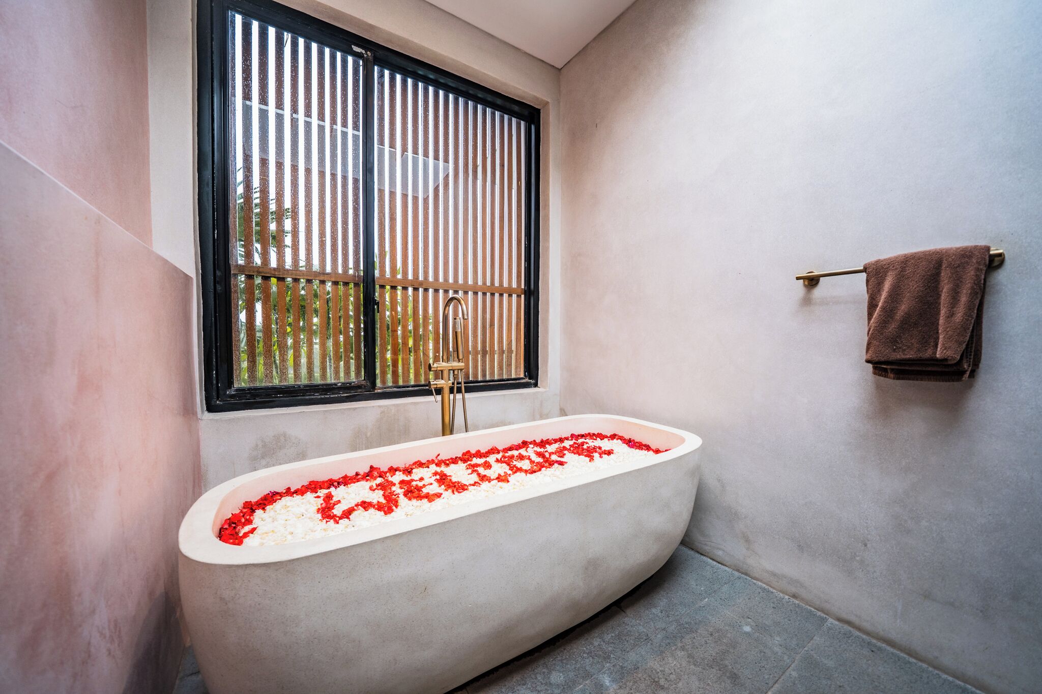 Een badkamer met een badkuip, een raam met verticale jaloezieën en een handdoekrek.