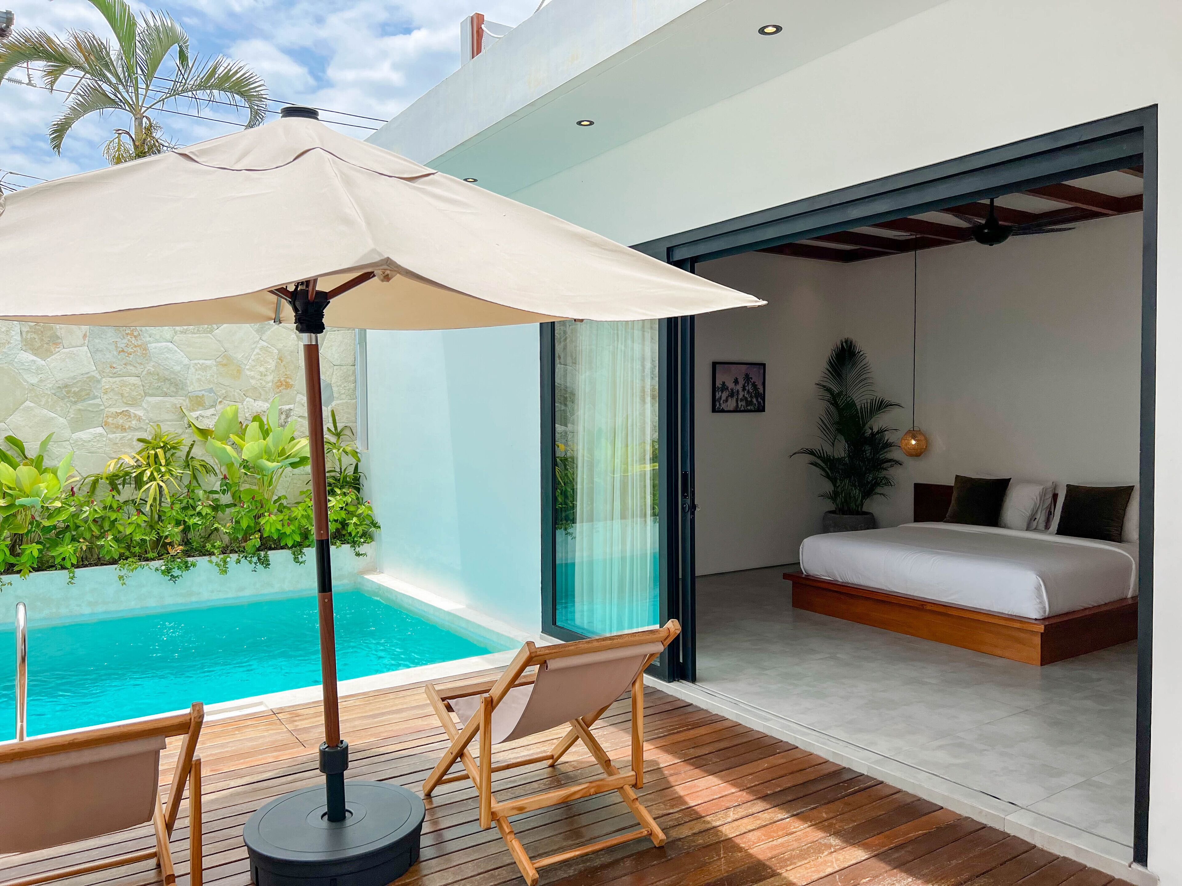 Une chambre moderne avec un grand lit, un petit balcon donnant sur une piscine et une terrasse en bois.