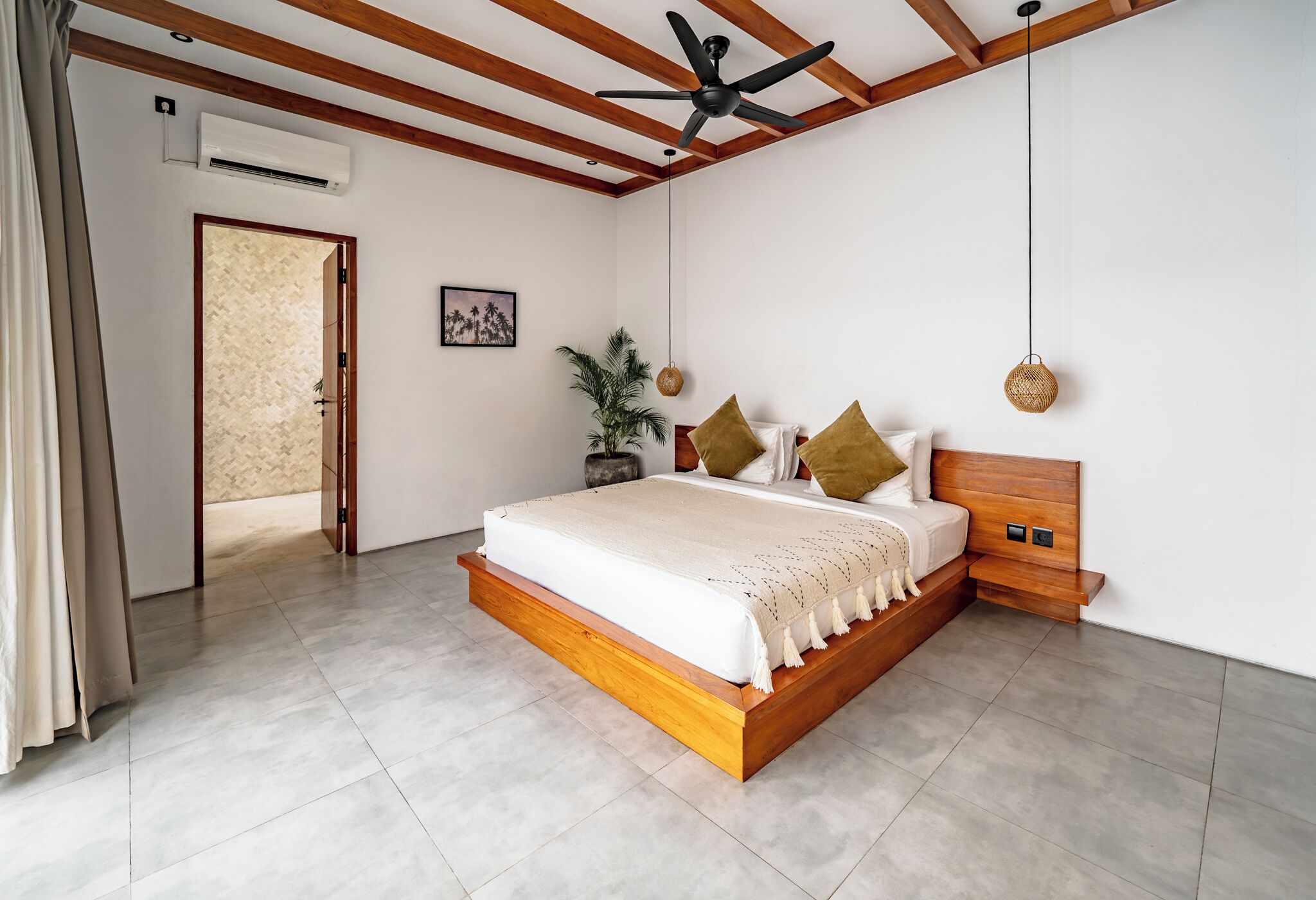 A bedroom with a wooden bed frame, a ceiling fan, a wall-mounted air conditioner, a door leading to another room, and a potted plant.
