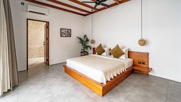 A bedroom with a wooden bed frame, a ceiling fan, a wall-mounted air conditioner, a door leading to another room, and a potted plant.