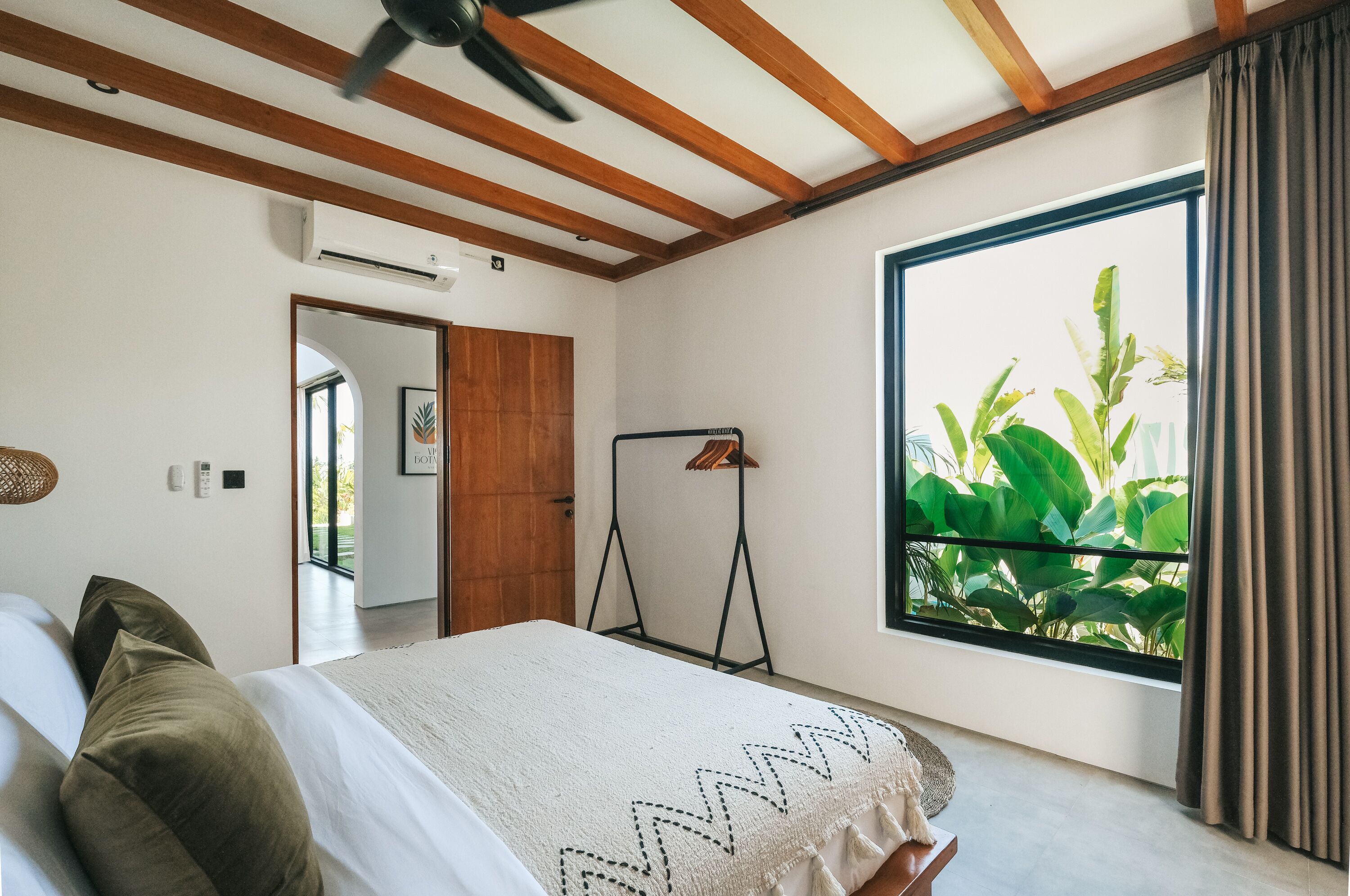 A bedroom with a bed, a ceiling fan, a window with curtains, and a view of greenery outside.