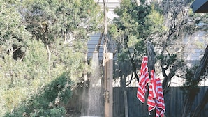 A garden with a concrete water feature, a wooden fence, and a tree with red and white striped cloths. - The back ultimate beach family, couples, girls trip or golf trip stay. (Blairgowrie)