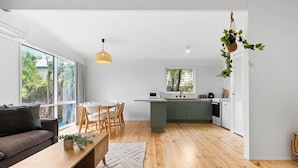 A modern kitchen with a central island, wooden flooring, and a dining area with a sofa and table. - The back ultimate beach family, couples, girls trip or golf trip stay. (Blairgowrie)