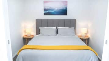 Une chambre à coucher comprenant un lit, deux lampes de chevet, une tête de lit et une œuvre d’art accrochée au mur.