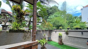 A covered patio area with a brick wall, potted plants, and a small water feature. - Sulendra Jungle Suites Ubud View by EPS (Ubud)