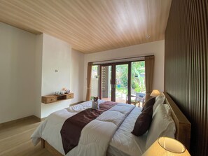 Un dormitorio con una cama grande, techo de madera, una ventana con cortinas y una mesita con objetos encima.