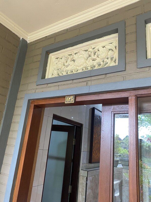 Una puerta con una placa de número, un panel decorativo en la pared y vistas al exterior.