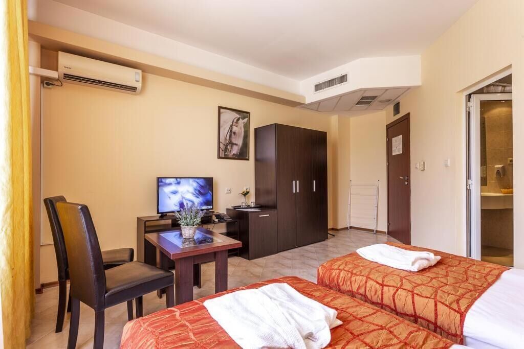 A hotel room with two beds, a desk with a television, a wardrobe, and an air conditioning unit.