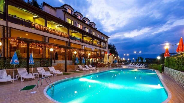 A hotel with a swimming pool, lounge chairs, and umbrellas.