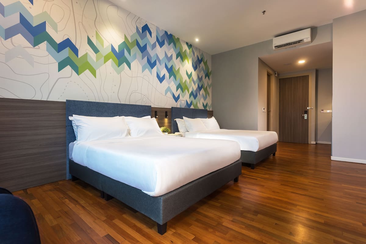 Une chambre d’hôtel avec deux lits, un plancher en bois et un mur orné d’un motif géométrique.
