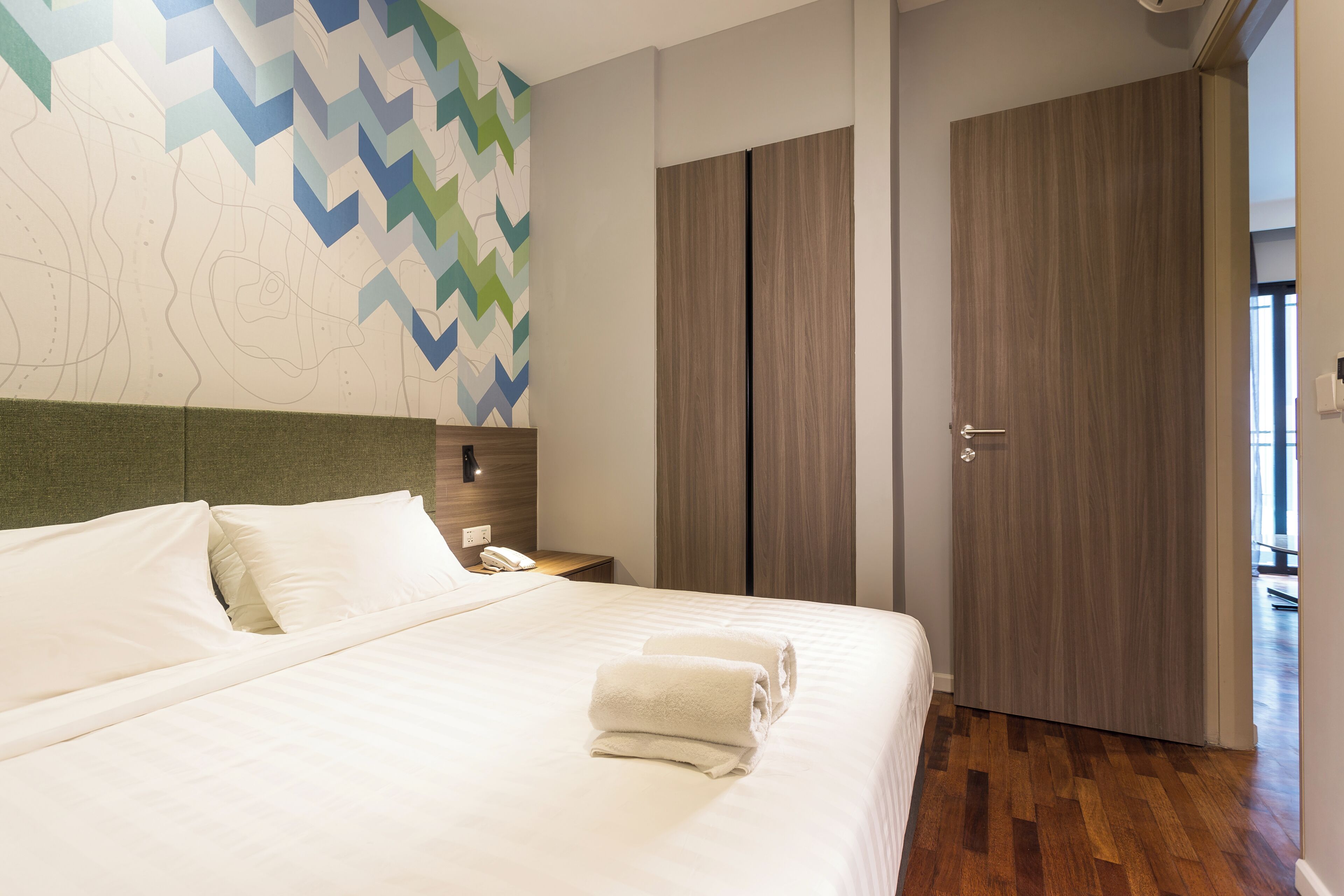 Una habitación de hotel con una cama, una mesita de noche, una pared con un diseño geométrico y un armario de madera.