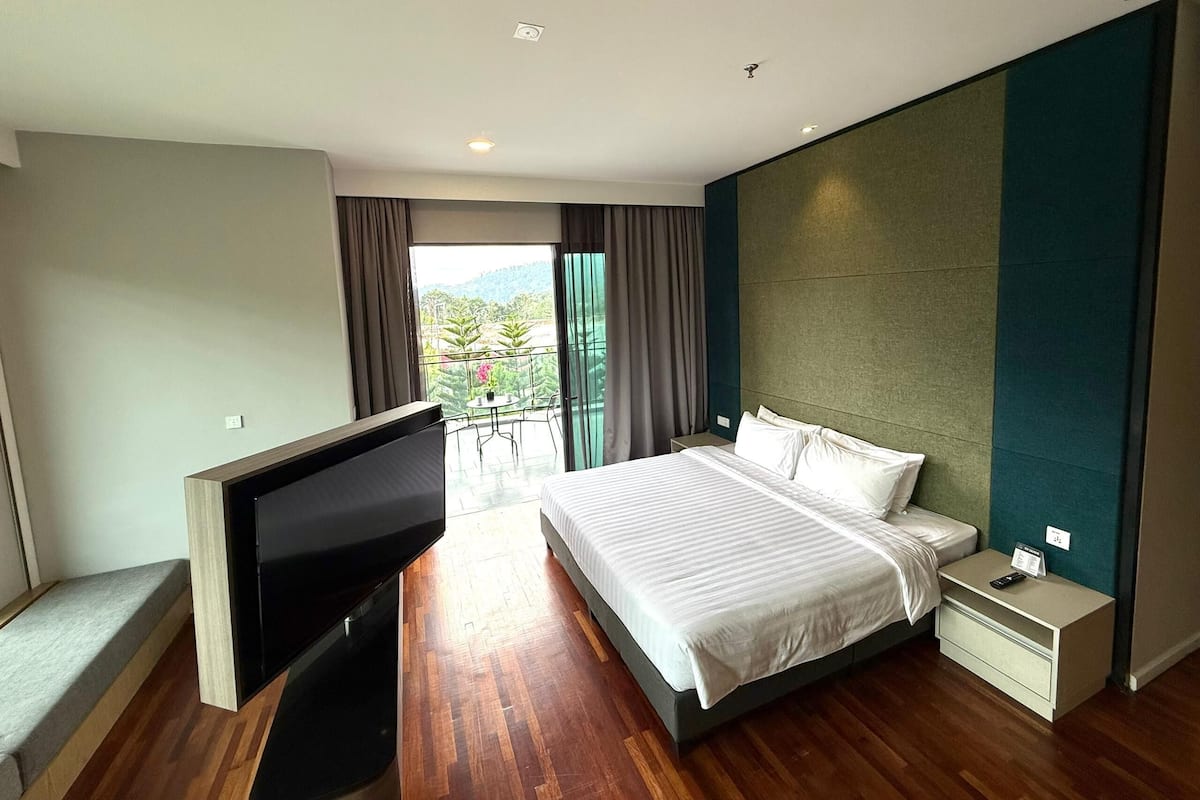 Une chambre d’hôtel moderne dotée d’un grand lit, d’une télévision, d’une table de chevet et d’un balcon offrant une vue sur la verdure.