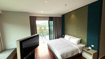 A modern hotel room with a large bed, a TV, a bedside table, and a balcony with a view of greenery.