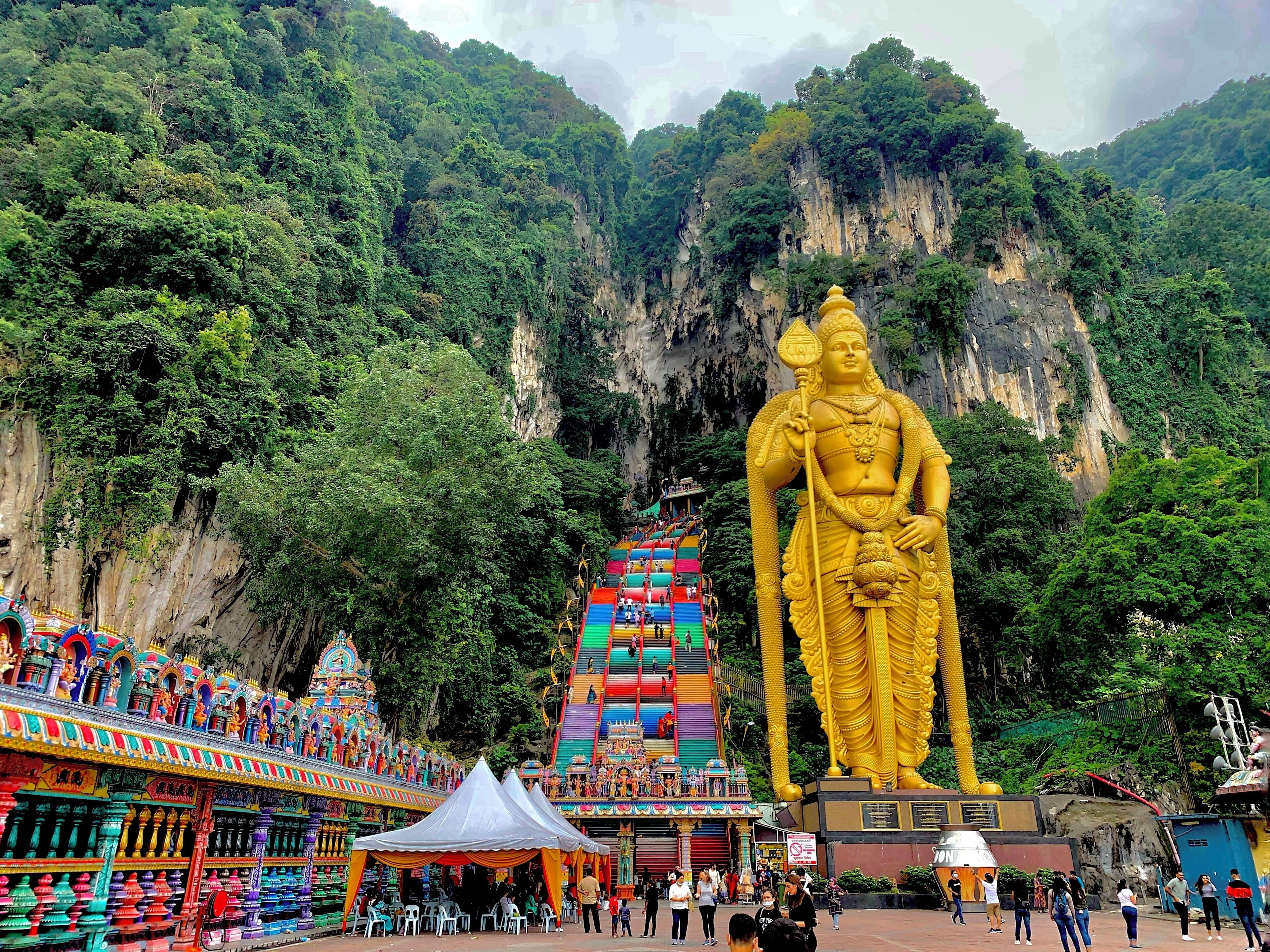 A large golden statue in front of a temple with colorful steps and a mountainous backdrop.