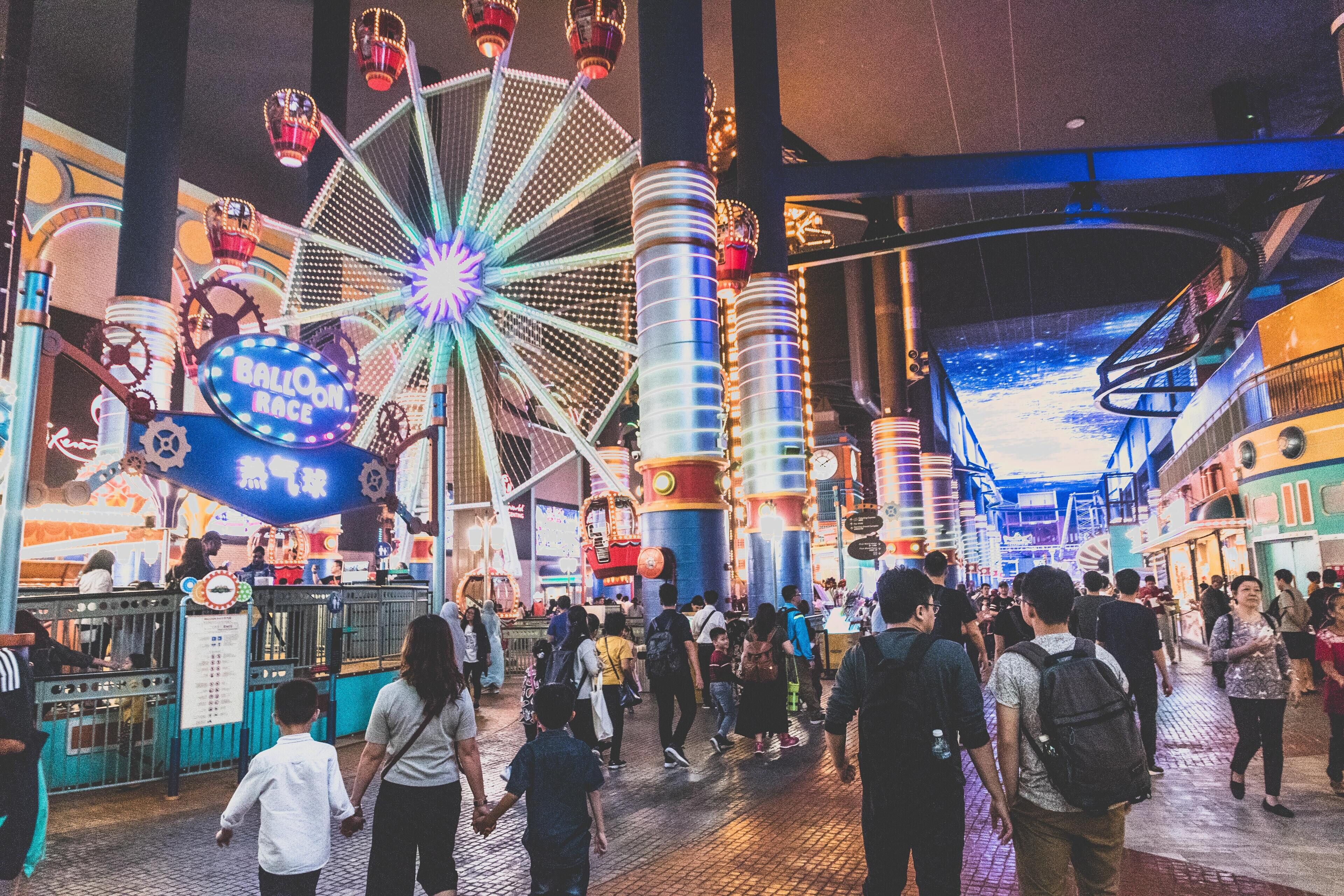 A bustling indoor amusement area with a Ferris wheel, various rides, and a crowd of people.