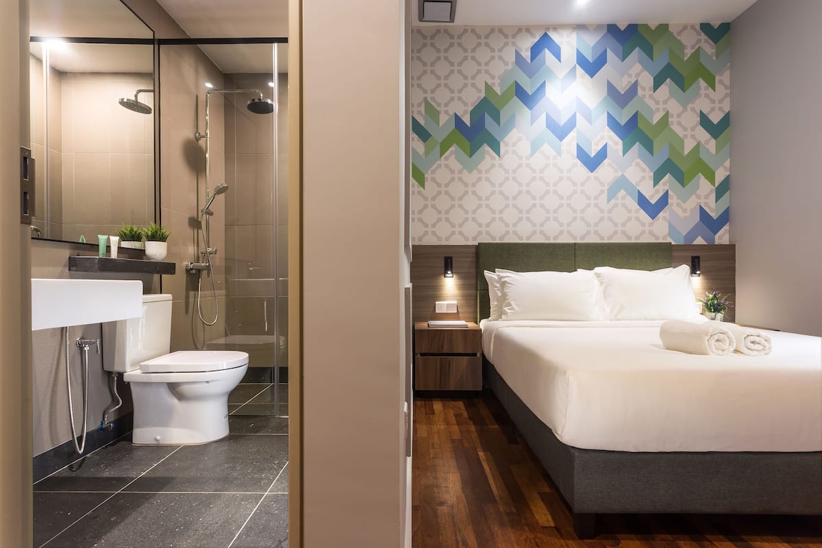 Une salle de bain moderne équipée d’une douche, de toilettes et d’un lavabo. La chambre comprend un lit avec du linge de lit blanc et un mur décoratif.