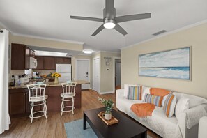 Una sala de estar moderna con un sofá blanco, una mesa de centro y una cocina con una mesa de comedor y sillas.