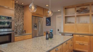 A modern kitchen with granite countertops, stainless steel appliances, wooden cabinets, and pendant lighting. - The Downtown Anchorage Grand Four Bedroom (Anchorage)