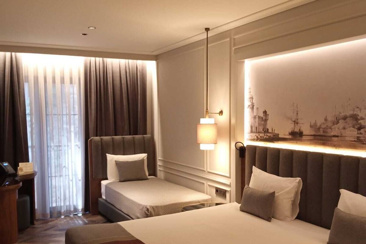 A hotel room with a large bed, two smaller beds, a desk, and a large window with curtains.