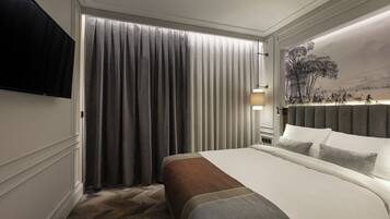 A hotel room with a large bed, a flat-screen TV, a painting on the wall, and a window with curtains.