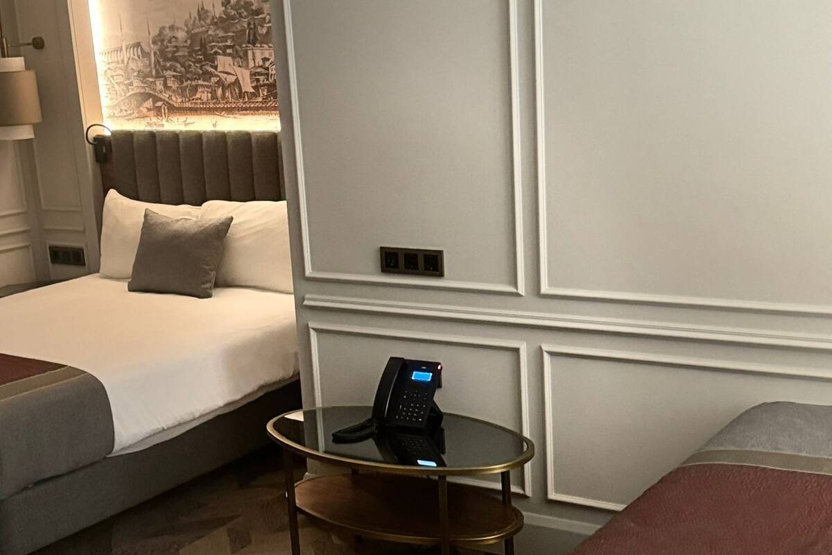 A hotel room with two beds, a bedside table with a phone, and a wall-mounted light.