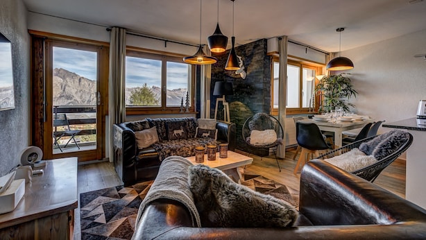 A spacious living room with a fireplace, leather sofas, a dining area, and large windows offering mountain views.