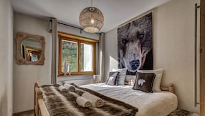 A bedroom with a large bed, a wooden headboard, a fur throw, and a wolf-themed painting.