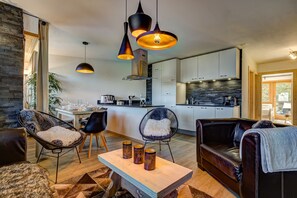 Uma sala de estar moderna com área de jantar, cozinha e parede de pedra decorativa.