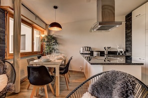 Una cocina moderna con zona de comedor, sillas de madera, una silla negra, una planta y una isla de cocina con pileta y cocina.